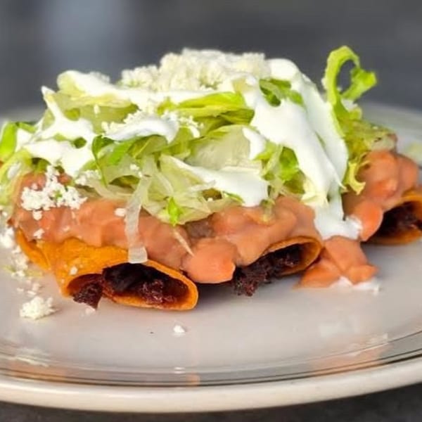 La Mex enchiladas topped with refried beans, shredded lettuce, sour cream, and crumbled cheese.
