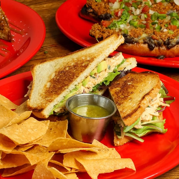 La Mex chicken salad sandwich with avocado, lettuce, chips, and salsa verde on a red plate.