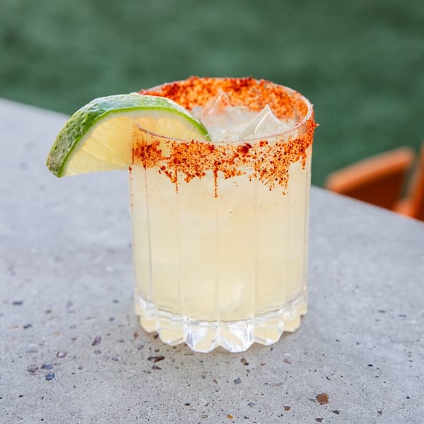 La Mex margarita with a chili-lime rim and a lime wedge, on a concrete surface.