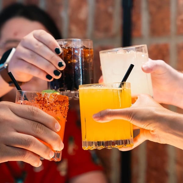 Four people toasting La Mex drinks: a margarita, a soda, a yellow cocktail, and a chili-rimmed drink.