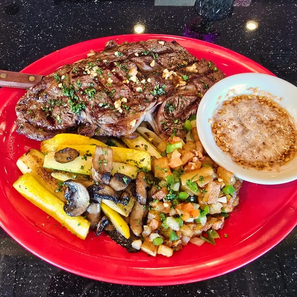 La Mex grilled steak with roasted vegetables, diced potatoes, and a side of sauce.